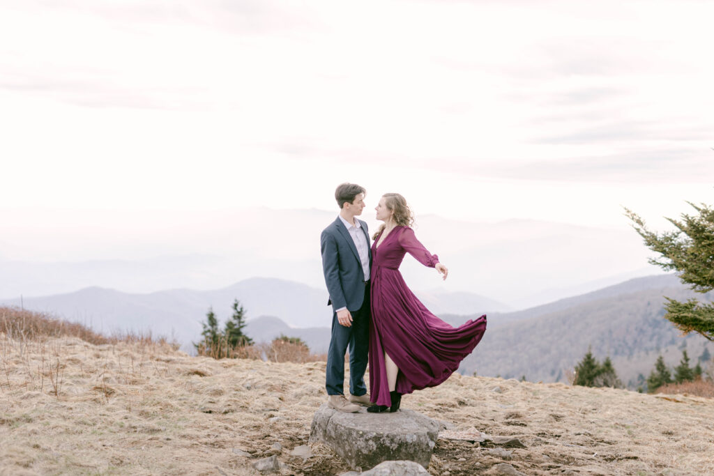 knoxville engagement photographer. couple standing on rock on top of roane mountain in tennesse. long dress flowing in the wind.