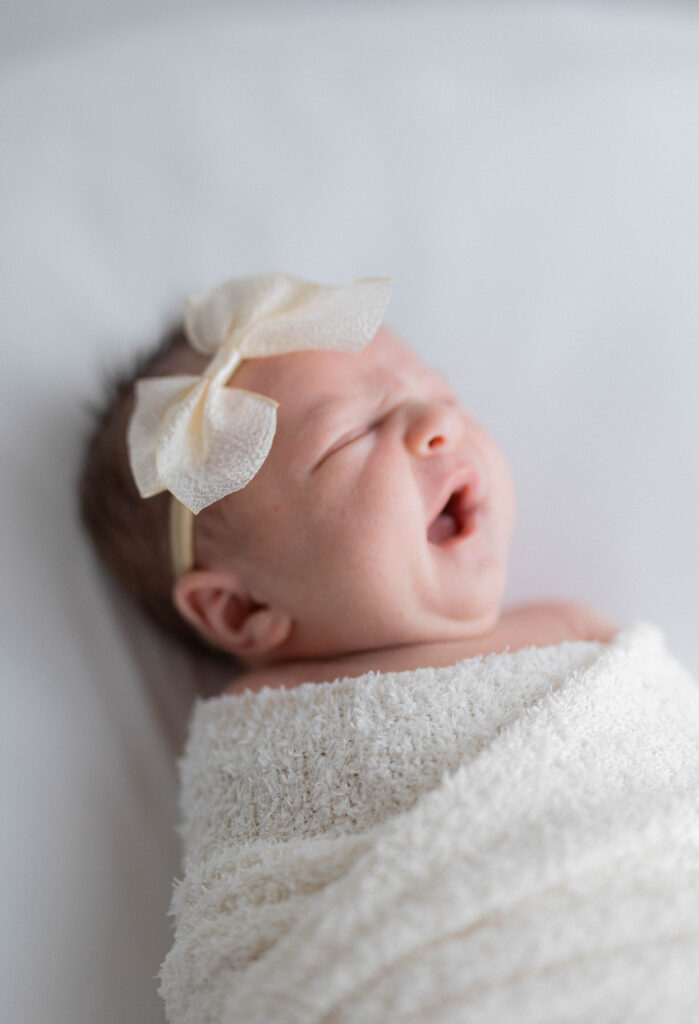 baby wrapped in white swaddle with white dainty bow yawning. Knoxville newborn photographers
