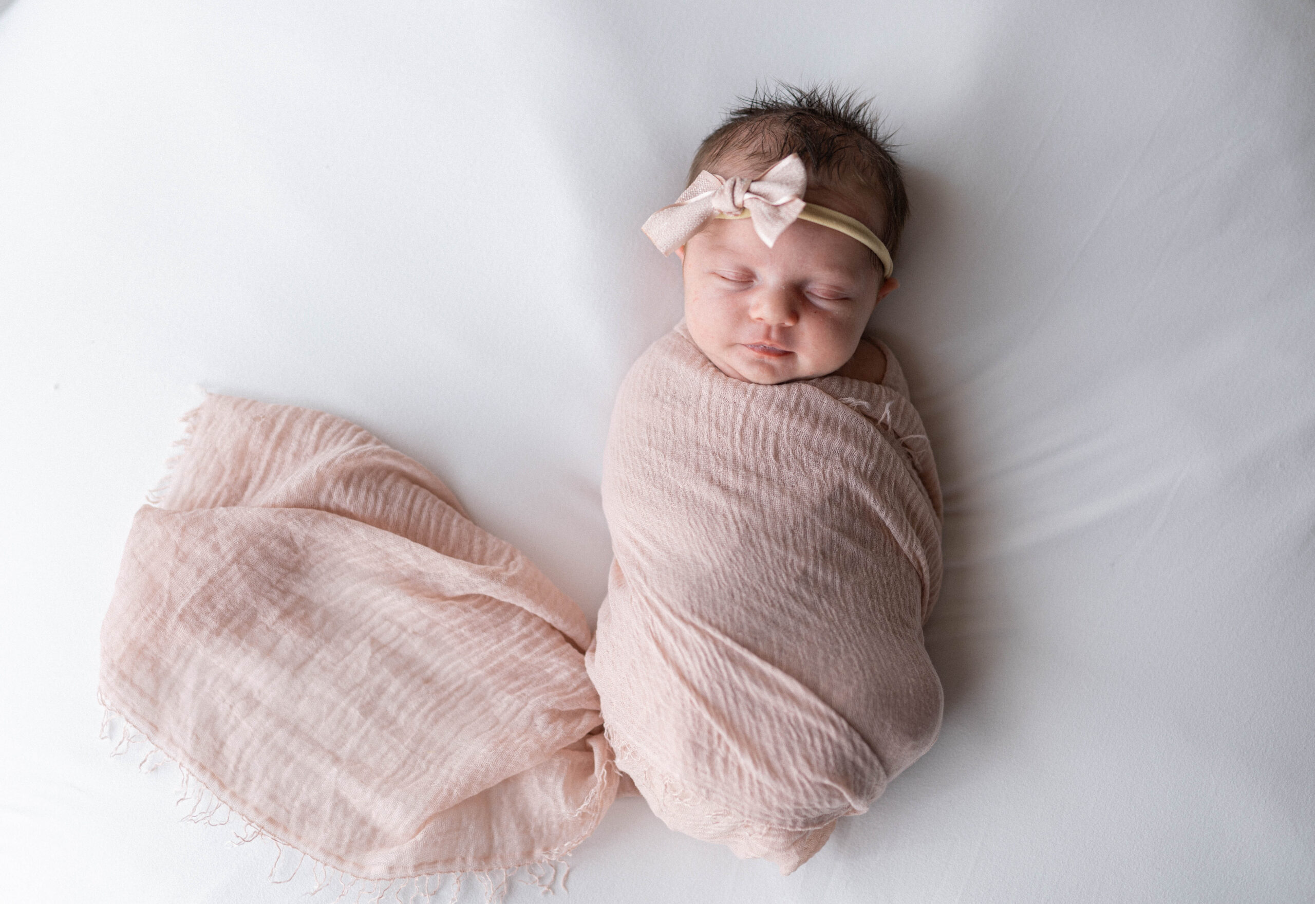 baby wrapped in pink gauze swaddle on white bed, sleeping. Knoxville newborn photographer