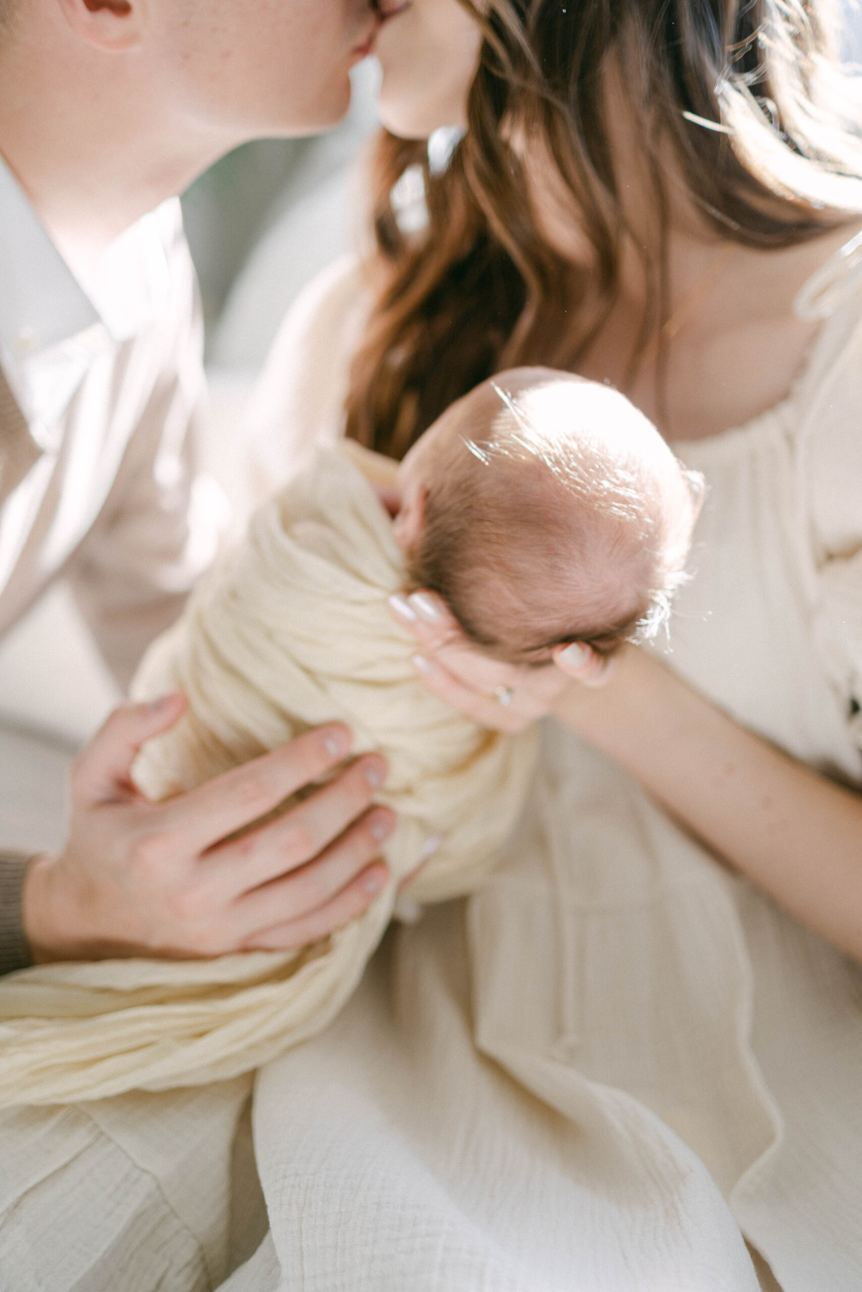 mom and dad holding swaddled baby in wrap. smiling at baby in bright window light. knoxville newborn photographer