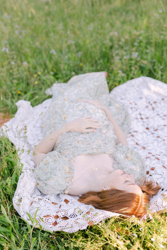 pregnant mom laying in a blanket in a field of green in a floral green pastel dress. knoxville maternity photographer